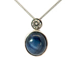 A silver chain necklace with a pendant featuring a round blue cabochon stone and a small clear round gemstone above it, set against a plain white background.