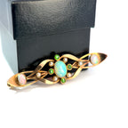 A gold-toned Art Deco brooch featuring a central iridescent blue opal, green gemstone accents, and small white pearls, displayed in front of a black jewelry box on a white background.