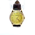A vintage-style wristwatch with a round gold-tone case, a pale yellow dial, and a dark brown textured leather strap, shown against a plain white background.